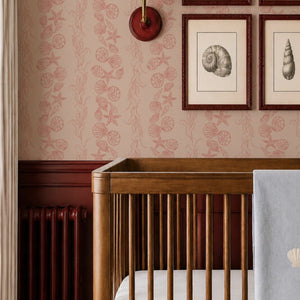 Bonnie wallpaper by Curate Space in red, seashells and seaweed in a stripe in a nursery with a wooden cot and framed shell prints
