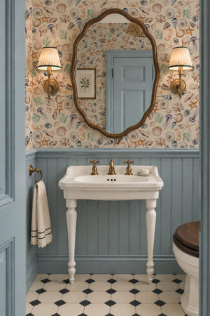 Charlotte Curate Space wallpaper in light cream, hand-painted seashells and starfish in a powder room with a pedestal basin and blue panelling
