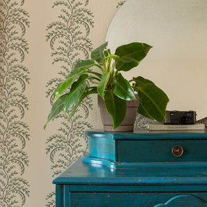 Edie wallpaper by Curate Space in soft green, arching fern fronds in vertical columns behind a teal chest of drawers and round mirror