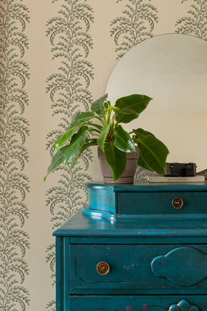 Edie wallpaper by Curate Space in soft green, arching fern fronds in vertical columns behind a teal chest of drawers and round mirror