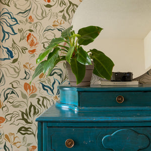 Eva wallpaper by Curate Space in off-white, a large-scale painterly floral in a room with a teal chest and a round mirror