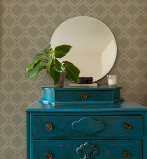 Florence wallpaper by Curate Space in lichen green, a leaf-lined diamond lattice behind a teal chest of drawers and round mirror