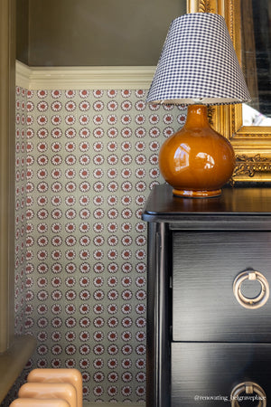 Mabel wallpaper by Curate Space in moss green, small rosette motifs in a hallway behind a black chest with a gingham lamp