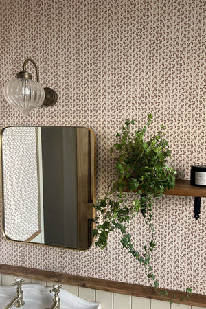 Maeva wallpaper by Curate Space in rouge red, a small trailing vine in a bathroom with a mirror and trailing plant