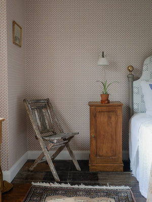 Maeva wallpaper by Curate Space in rouge red, a small trailing vine in a bedroom corner with a folding chair