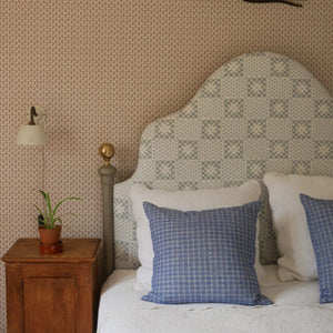 Maeva wallpaper by Curate Space in rouge red, a small trailing vine in a bedroom with an upholstered headboard and a wooden bedside table