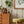 Olive Curate Space wallpaper in light cream, vertical stripes of botanical stems and wildflowers in a room with a mid-century chest, a yellow stool and a plant