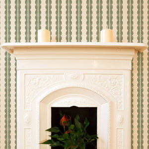 Rosalie wallpaper by Curate Space in soft green, a scalloped stripe in a room with a fireplace and a potted plant