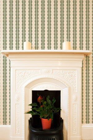 Rosalie wallpaper by Curate Space in soft green, a scalloped stripe in a room with a fireplace and a potted plant