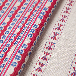 Wild Flower linen by Bethie Tricks in red and blue, draped close-up beside a red and blue scalloped stripe fabric